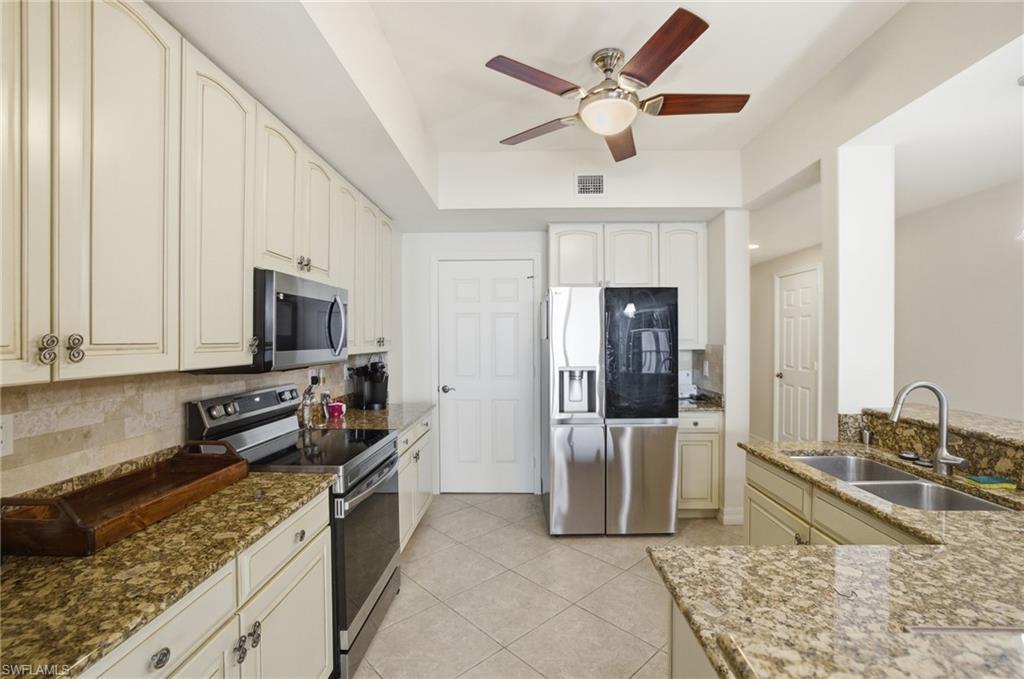 Kitchen featuring appliances with stainless steel finishes, backsplash, light stone countertops, and light tile patterned floors