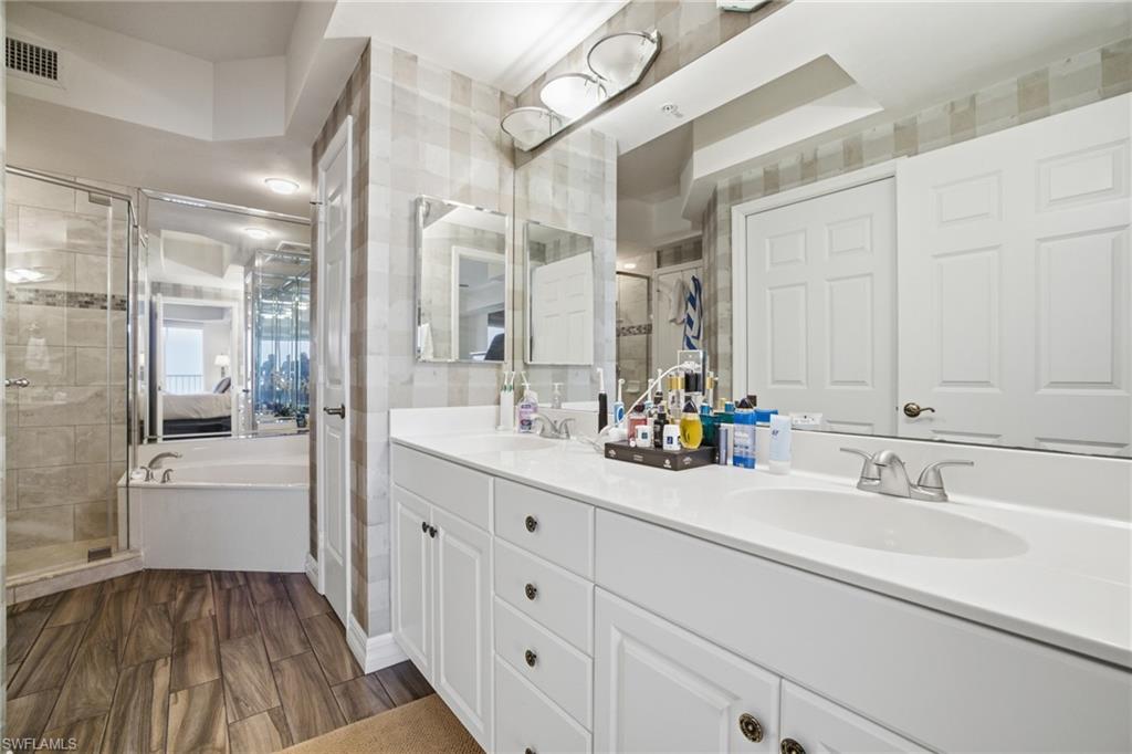 Bathroom with double vanity, wood tiled floors, a garden tub, a shower stall, and tile walls