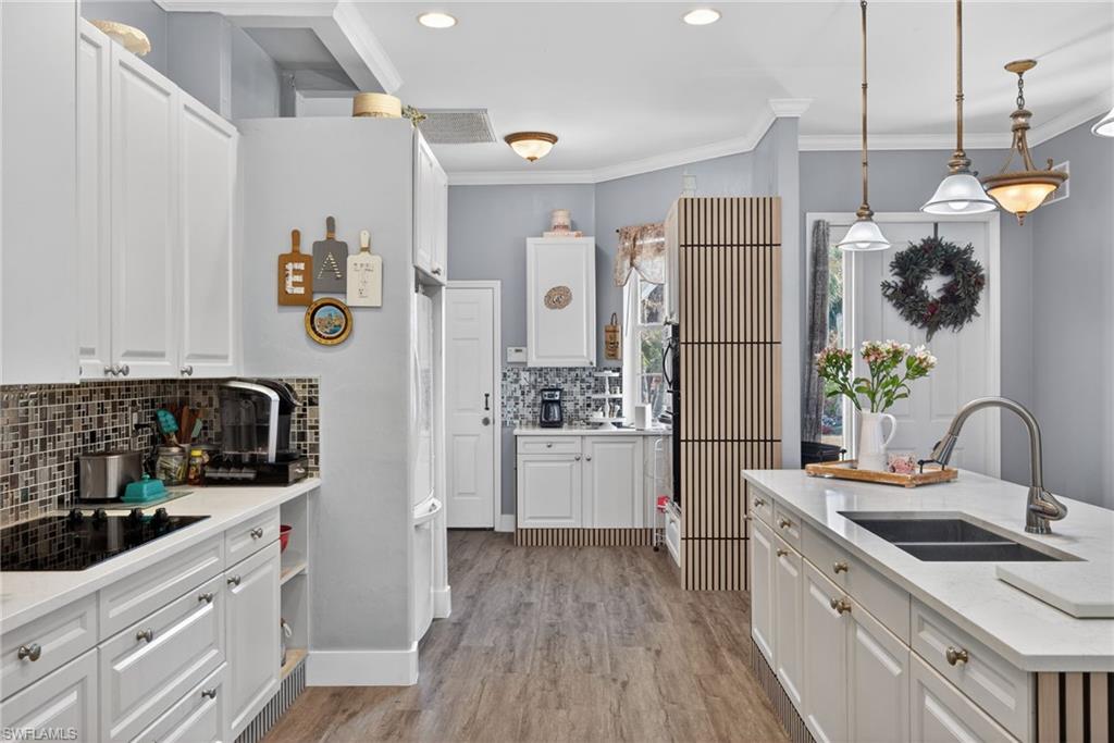 Kitchen with backsplash, white cabinets, crown molding, pendant lighting, and black electric stovetop
