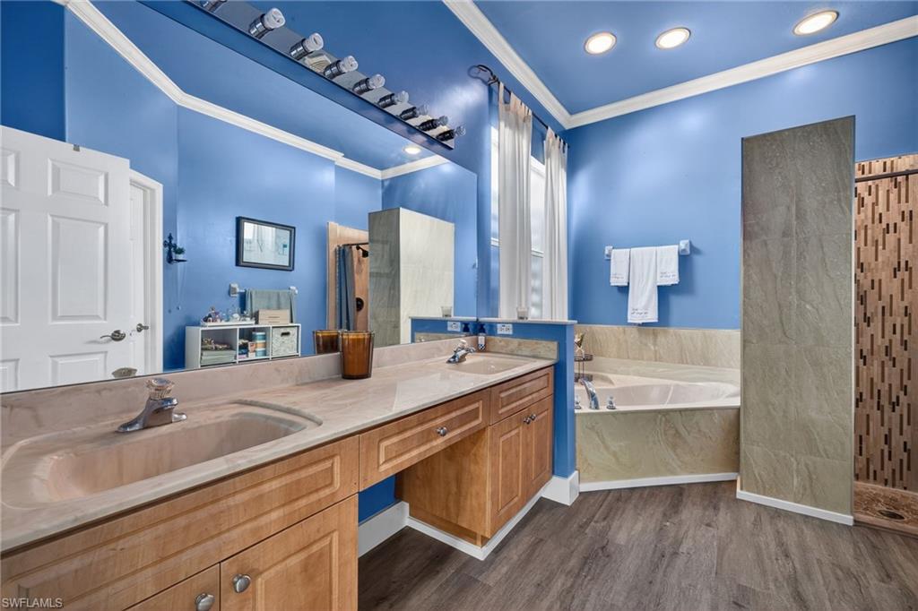 Full bath with a walk in shower, a garden tub, double vanity, dark wood-style flooring, and crown molding
