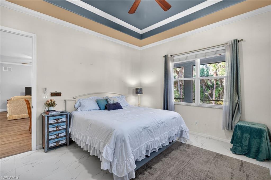Bedroom featuring marble look tiles, crown molding, a ceiling fan, and a tray ceiling