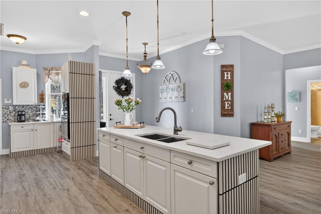 Kitchen featuring ornamental molding, hanging light fixtures, white cabinetry, light stone counters, and a kitchen island with sink