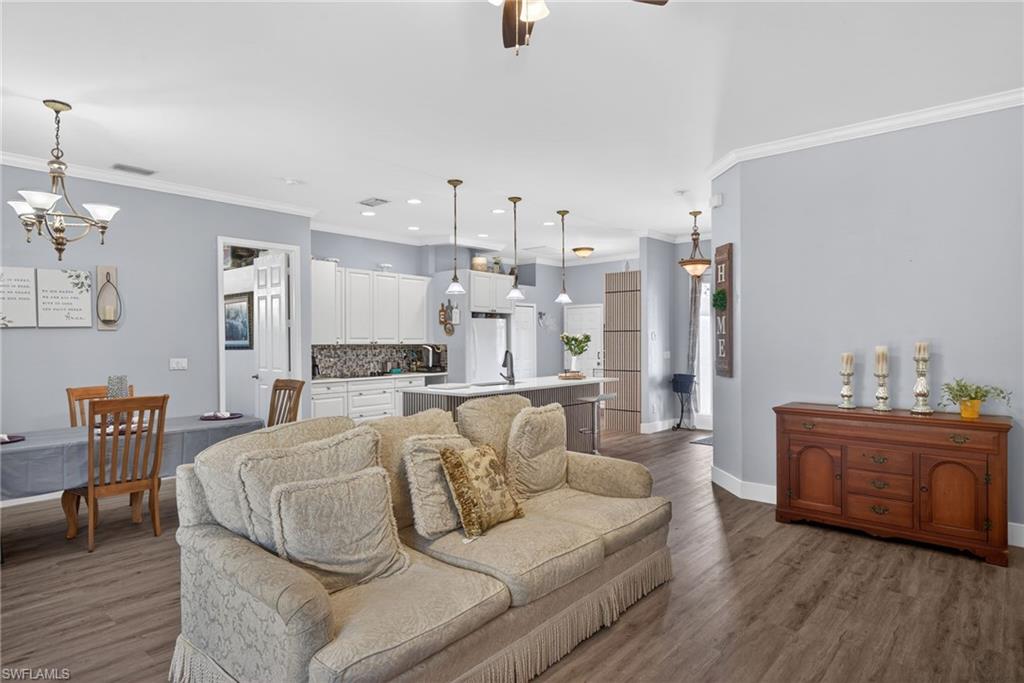 Living room featuring ornamental molding, hanging lights, dark wood-style floors, and ceiling fan