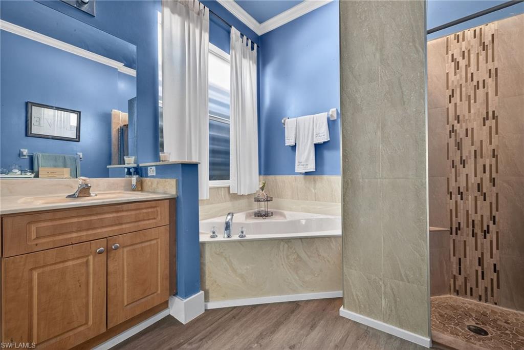 Full bathroom with vanity, a garden tub, crown molding, a tile shower, and dark wood-style floors