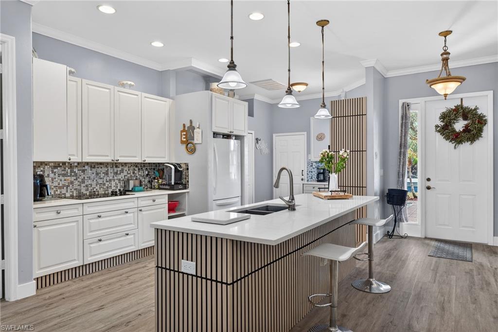 Kitchen with a kitchen breakfast bar, crown molding, white cabinetry, light wood finished floors, and pendant lighting