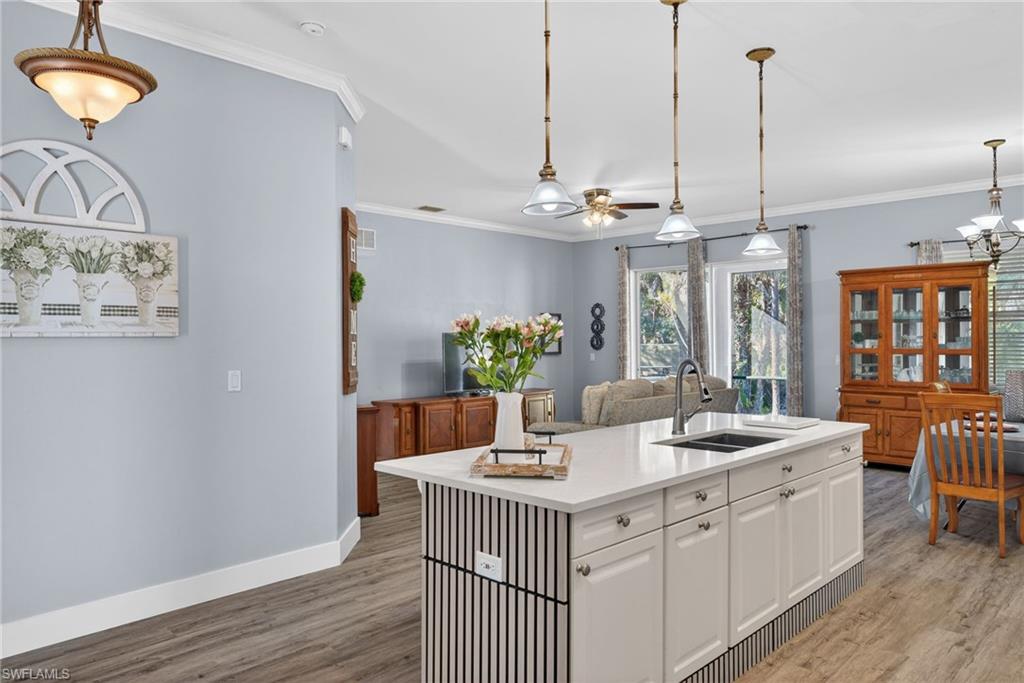 Kitchen with white cabinetry, crown molding, an island with sink, light wood-style flooring, and a ceiling fan
