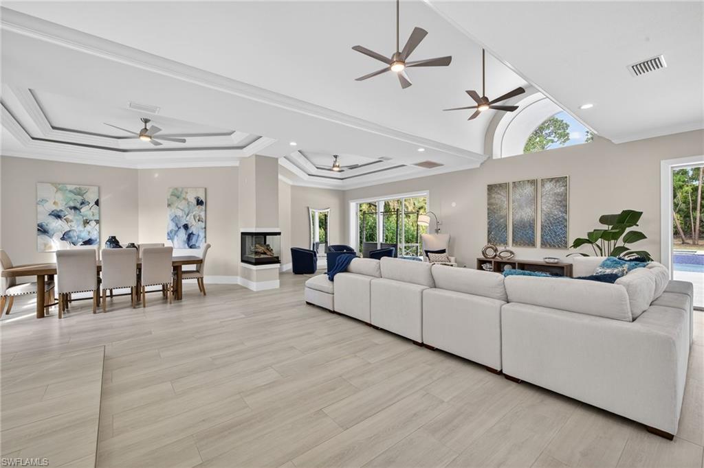 Living area with a ceiling fan, ornamental molding, light wood finished floors, a multi sided fireplace, and a raised ceiling