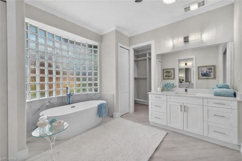 Full bath with a soaking tub, vanity, crown molding, a spacious closet, and tile walls