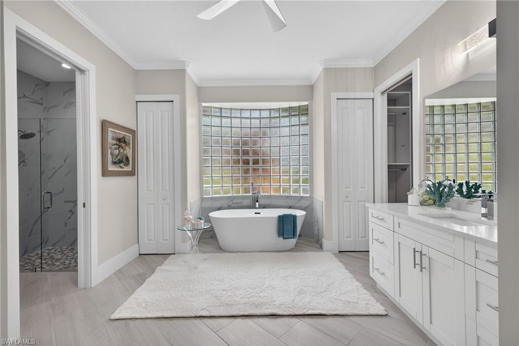 Bathroom with a marble finish shower, a soaking tub, a ceiling fan, vanity, and ornamental molding