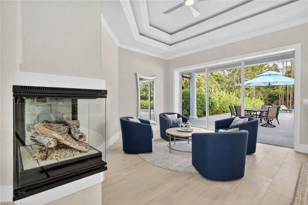 Living room with a tray ceiling, wood finished floors, a ceiling fan, ornamental molding, and a glass covered fireplace