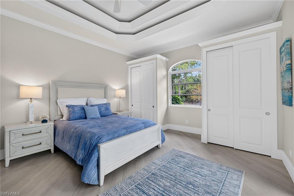 Bedroom with multiple closets, ornamental molding, light wood finished floors, a raised ceiling, and a ceiling fan