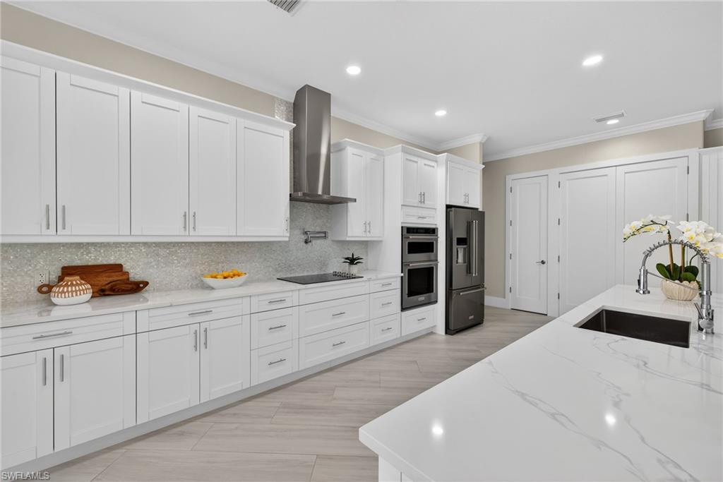 Kitchen with light stone countertops, white cabinets, stainless steel appliances, backsplash, and crown molding