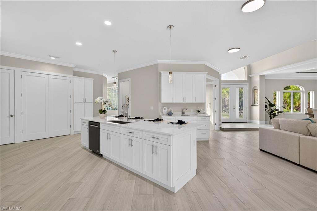 Kitchen featuring open floor plan, decorative light fixtures, white cabinets, a center island with sink, and light wood-style floors