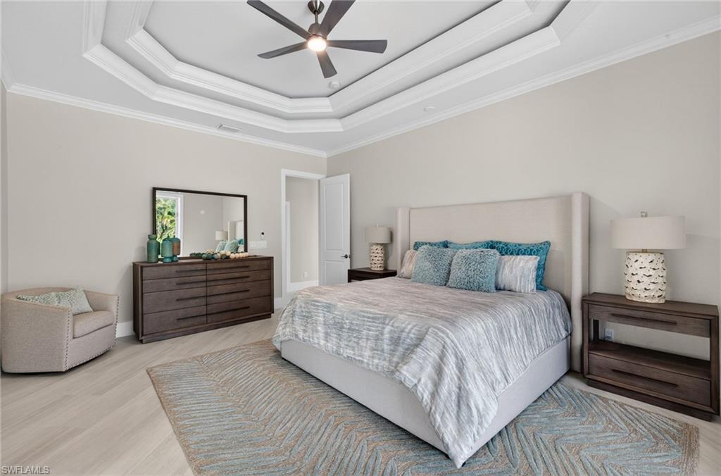 Bedroom with crown molding, light wood-type flooring, ceiling fan, and a tray ceiling