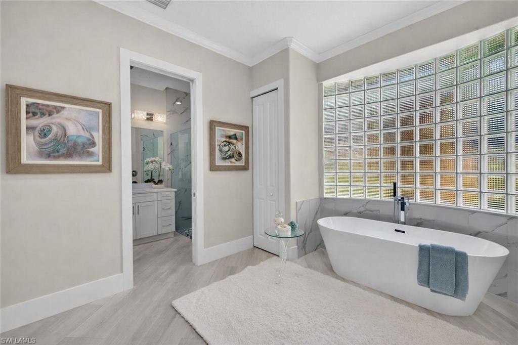 Full bath featuring a soaking tub, ornamental molding, light wood-style flooring, vanity, and healthy amount of natural light