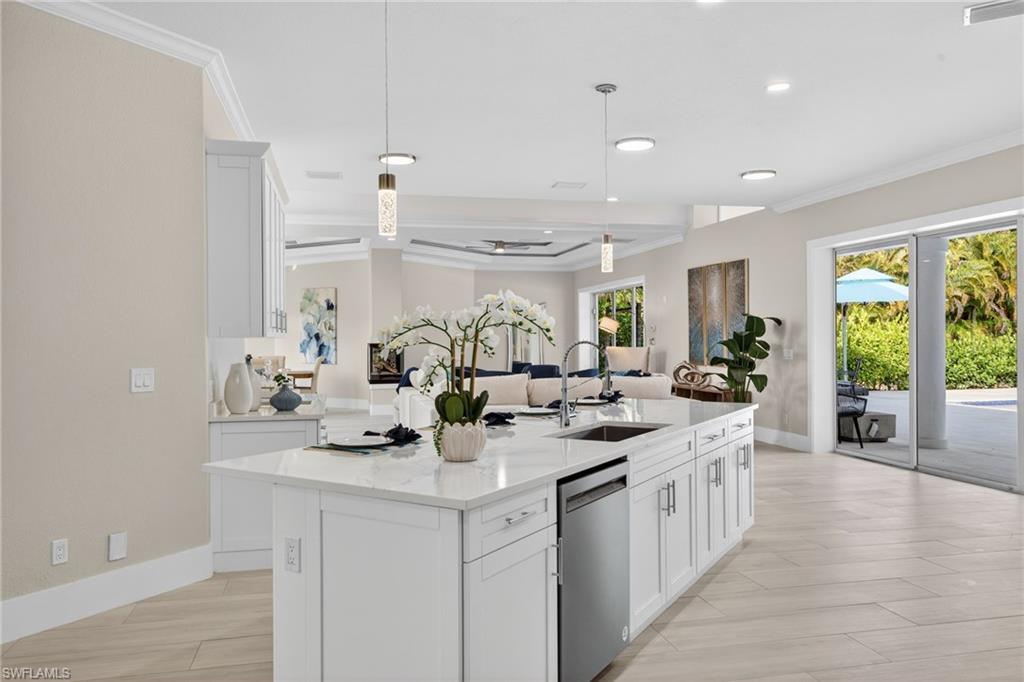 Kitchen featuring white cabinetry, ornamental molding, light stone countertops, pendant lighting, and stainless steel dishwasher