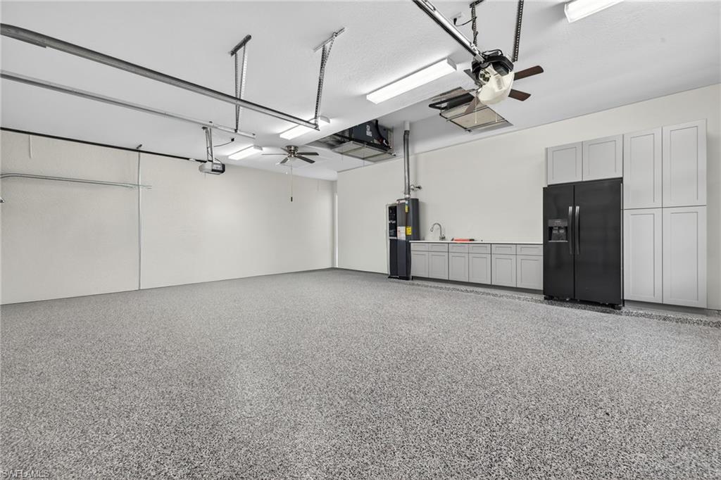 Garage with a ceiling fan, black refrigerator with ice dispenser, and water heater