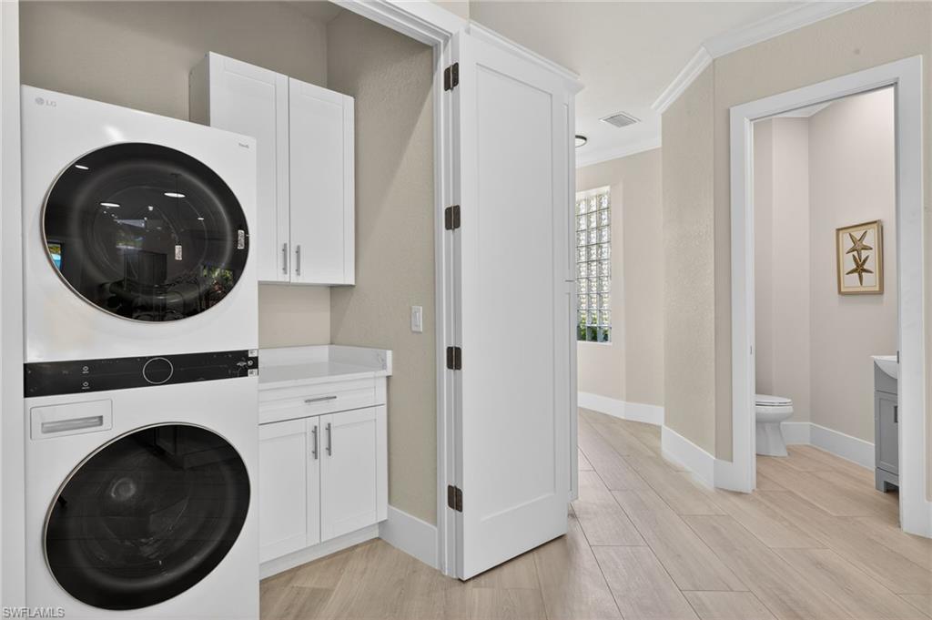 Laundry room with crown molding, stacked washer and clothes dryer, light wood-type flooring, and cabinet space