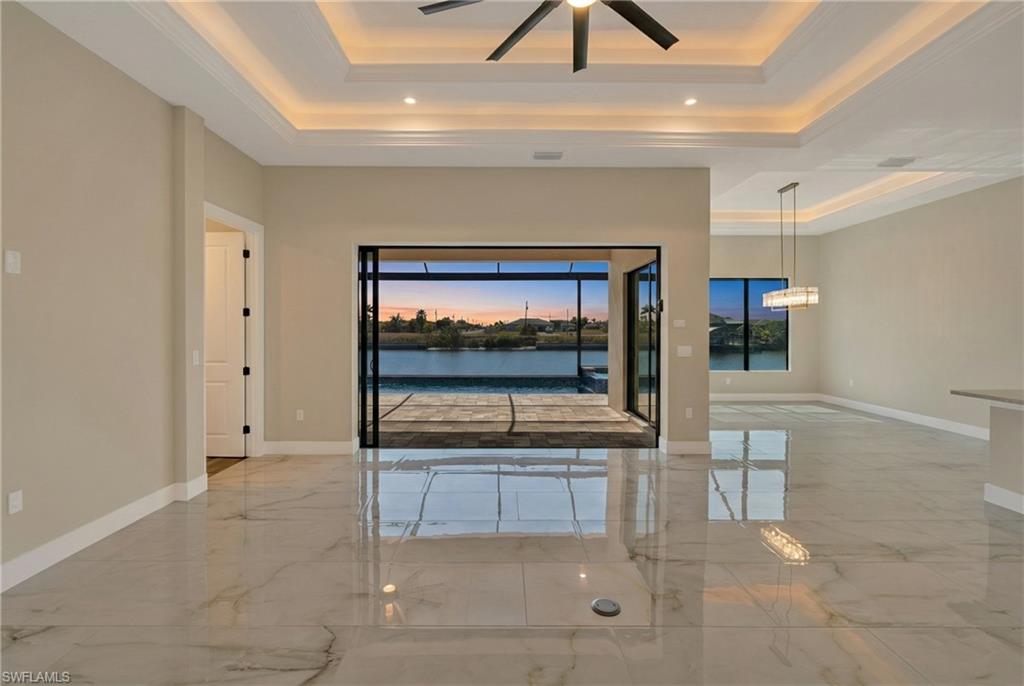 Empty room featuring plenty of natural light, light marble finish flooring, a ceiling fan, and a tray ceiling
