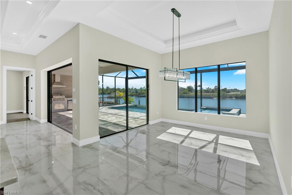 Unfurnished dining area with a sunroom, a tray ceiling, light marble finish floors, and a water view