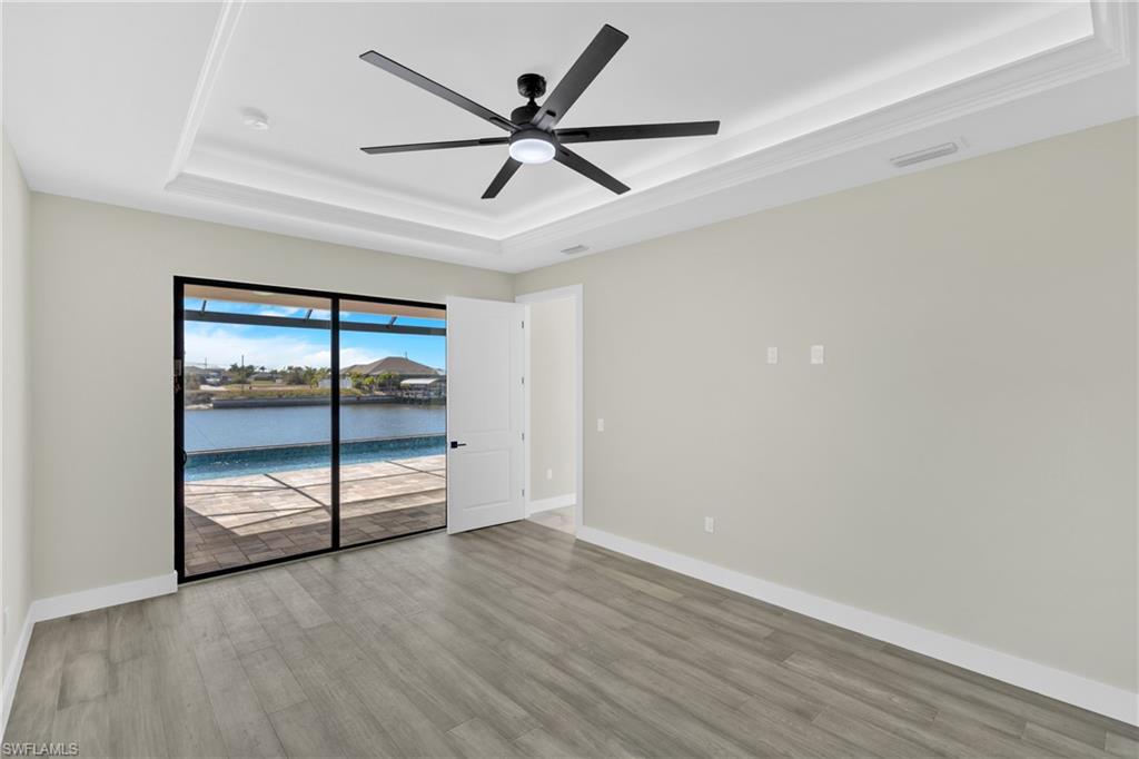 Unfurnished room featuring a tray ceiling, ceiling fan, light wood-style flooring, a water view, and a sunroom