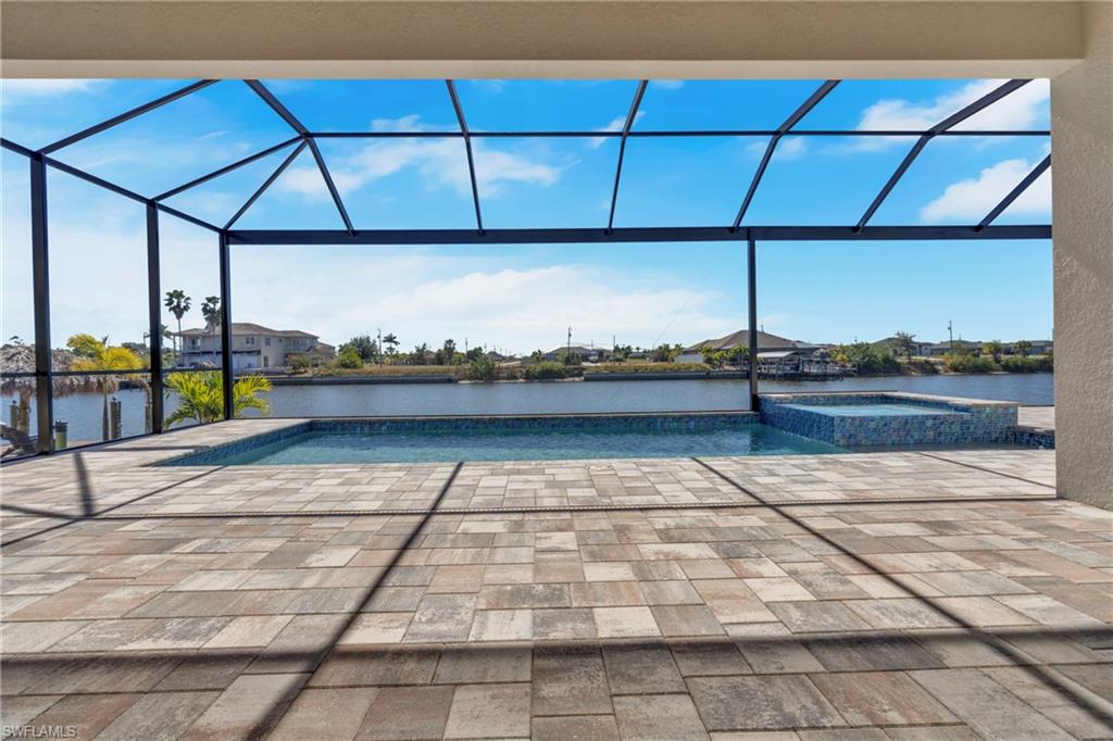 Integrated pool / hot tub featuring glass enclosure, a sunroom, a water view, and a patio area