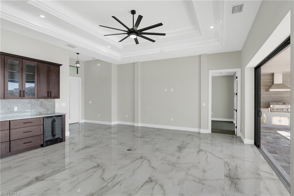 Unfurnished living room featuring wine cooler, a ceiling fan, recessed lighting, light marble finish floors, and a tray ceiling