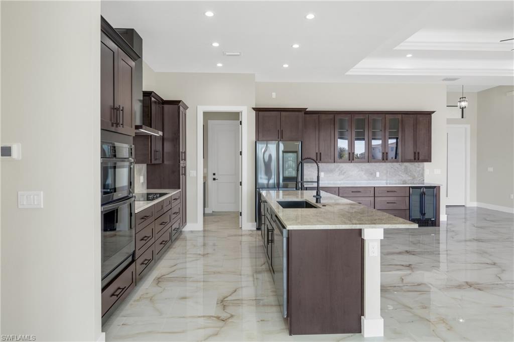 Kitchen with glass fronted cabinets, light stone countertops, a tray ceiling, dark wood finish cabinets, and hanging light fixtures