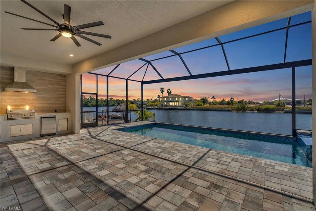 Swimming pool with exterior kitchen, a sunroom, a patio area, glass enclosure, and a water view