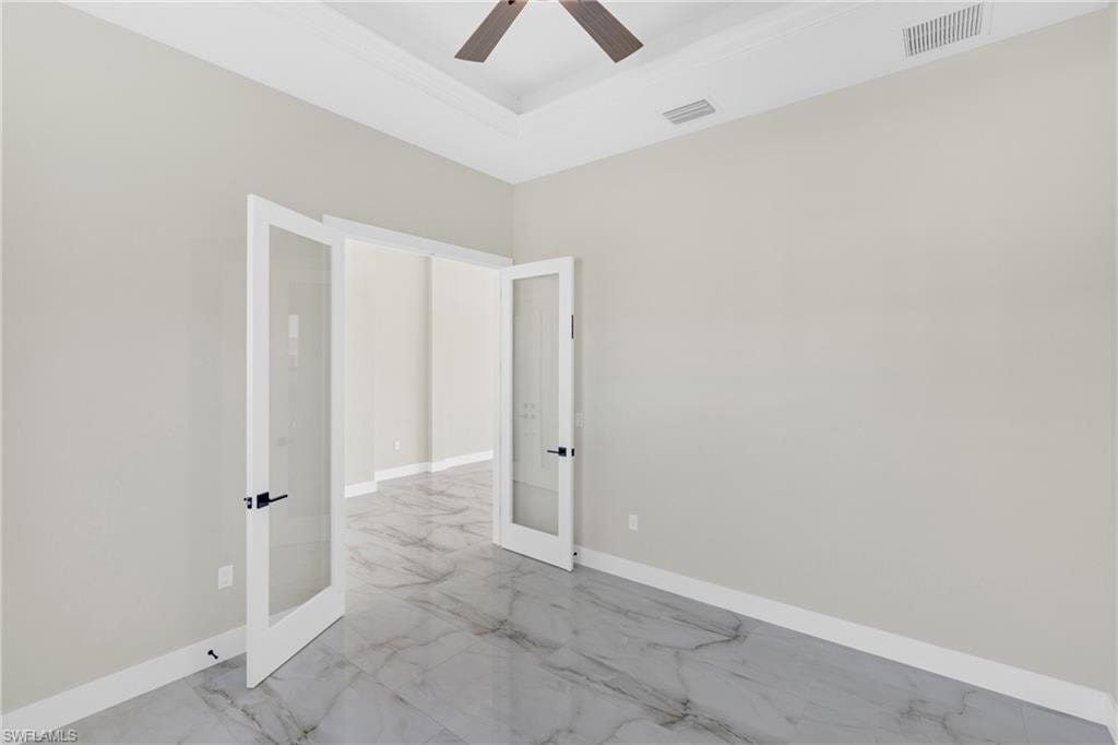 Spare room with french doors, a ceiling fan, a raised ceiling, and light marble finish flooring