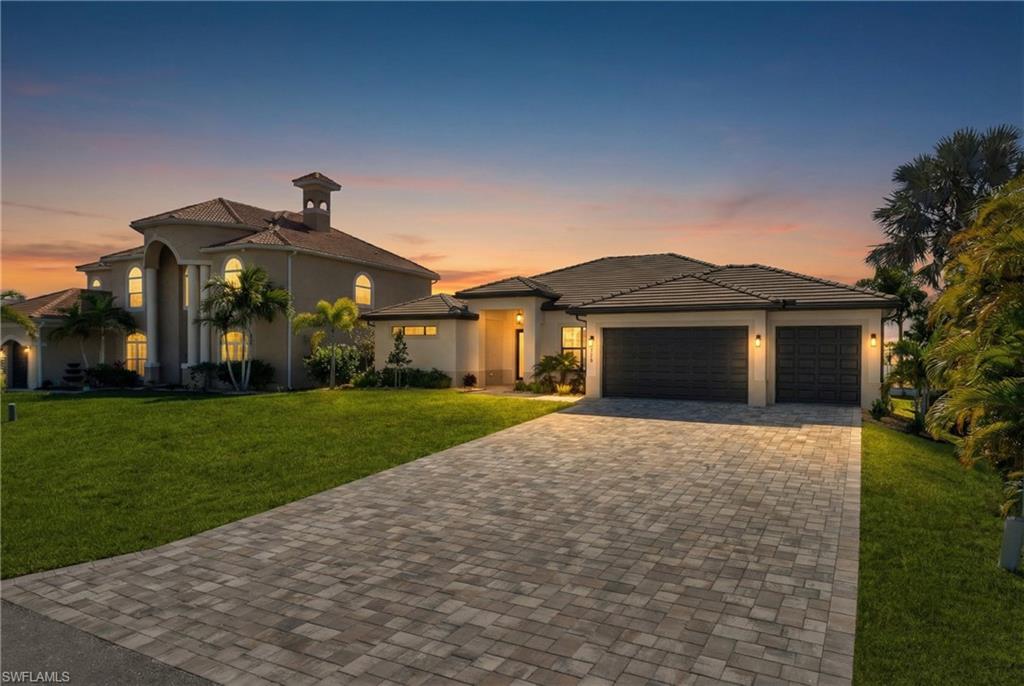 View of front of house featuring a yard, decorative driveway, stucco siding, and an attached garage