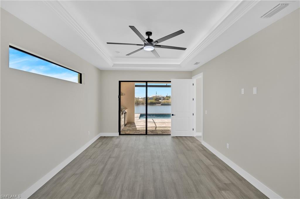 Empty room featuring ceiling fan, light wood-style flooring, a water view, and a raised ceiling
