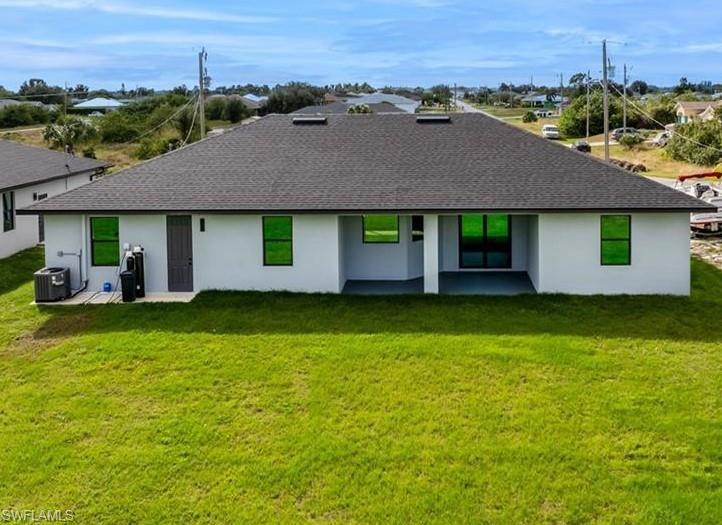 Back of property featuring stucco siding, roof with shingles, a patio, and a yard