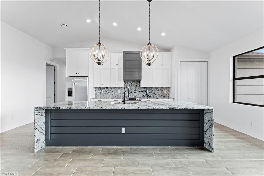 Kitchen with light stone countertops, white cabinetry, stainless steel refrigerator with ice dispenser, a spacious island, and lofted ceiling