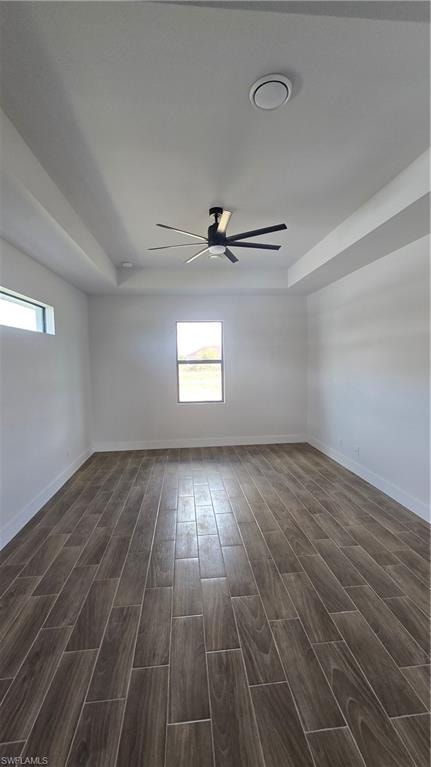 Empty room with a ceiling fan, wood finish floors, and a tray ceiling