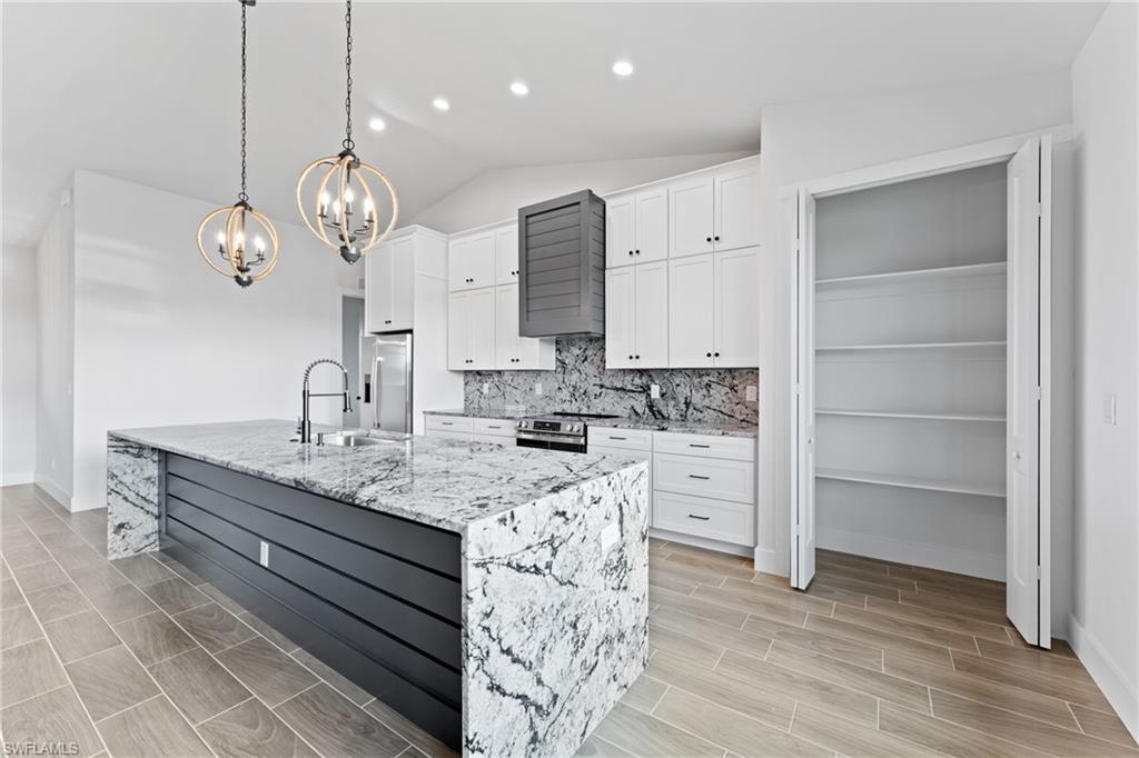 Kitchen featuring white cabinetry, hanging lights, decorative backsplash, light stone countertops, and vaulted ceiling