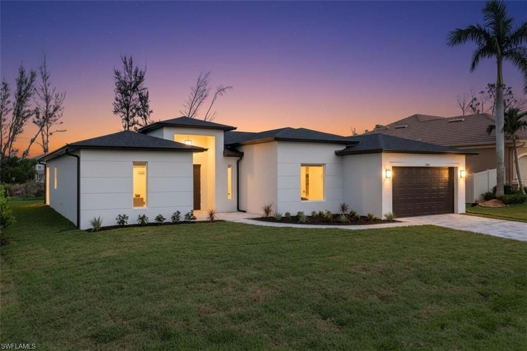 View of front of property with a yard, driveway, a garage, and stucco siding