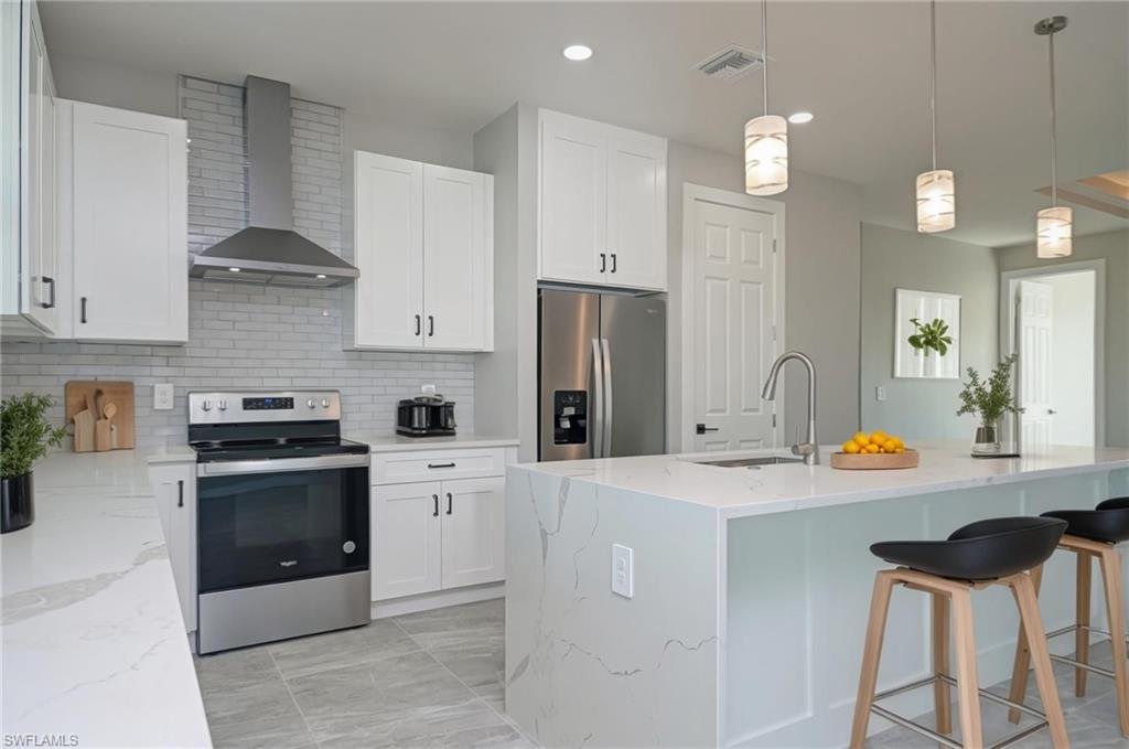 Kitchen featuring stainless steel appliances, pendant lighting, light stone countertops, a kitchen bar, and white cabinetry