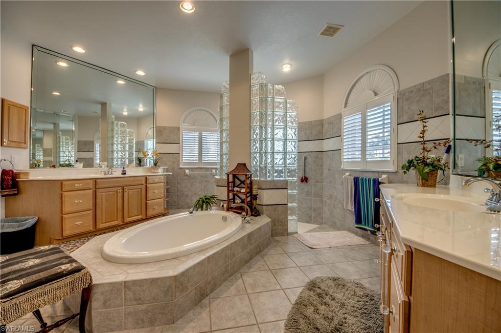 Bathroom featuring two vanities, a bath, walk in shower, light tile patterned flooring, and healthy amount of natural light