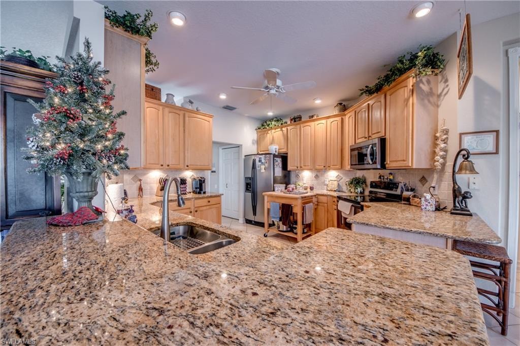 Kitchen with stainless steel appliances, light stone countertops, light wood finish cabinets, ceiling fan, and recessed lighting