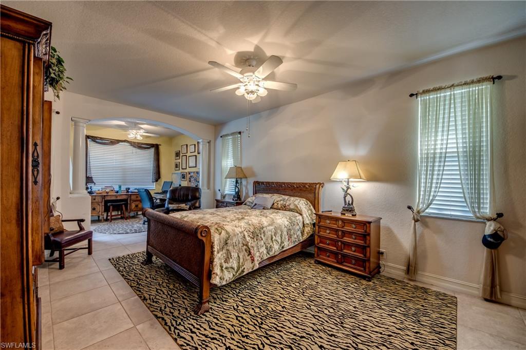 Bedroom featuring a ceiling fan, light tile patterned flooring, arched walkways, and multiple windows