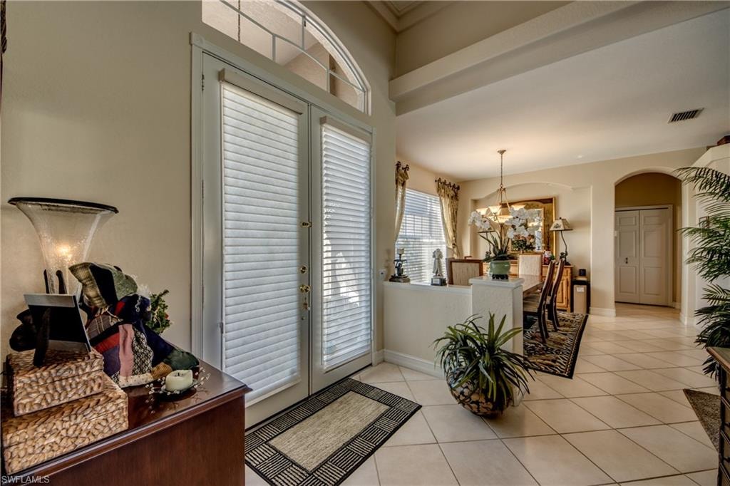 Entrance foyer featuring french doors, arched walkways, light tile patterned floors, and suspended lighting