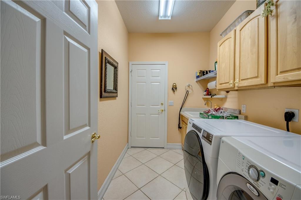 Laundry room featuring washer and clothes dryer, light tile patterned flooring, and cabinet space
