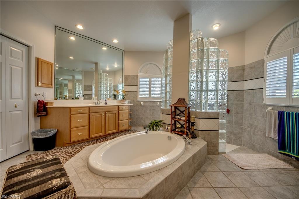 Bathroom featuring vanity, walk in shower, a garden tub, light tile patterned floors, and recessed lighting
