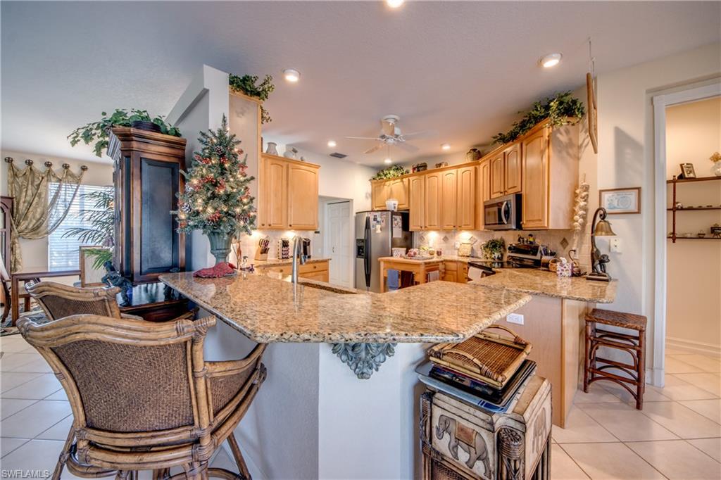 Kitchen with light tile patterned flooring, a breakfast bar, light wood finish cabinetry, stainless steel appliances, and recessed lighting