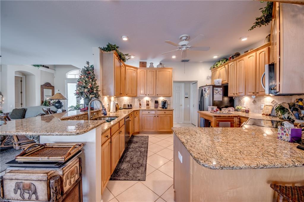 Kitchen with a peninsula, a kitchen breakfast bar, light stone countertops, open floor plan, and light wood finish cabinets