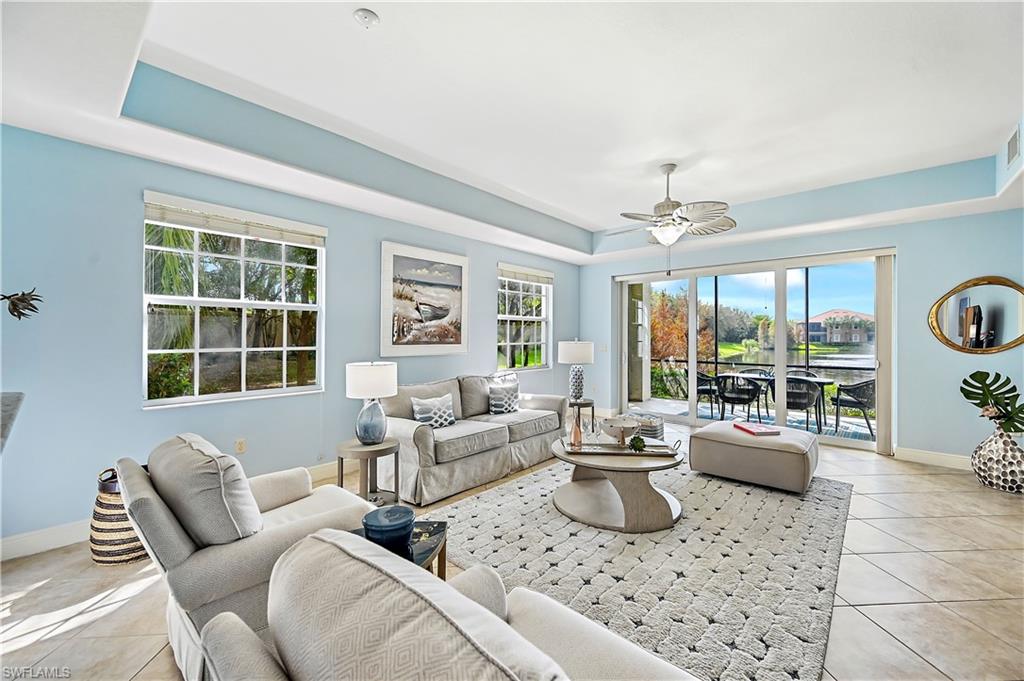 Living room with a raised ceiling, light tile patterned floors, and ceiling fan