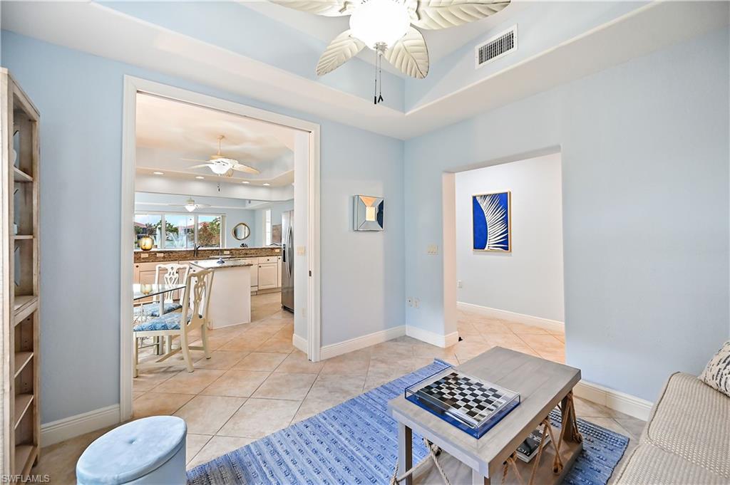 Living room with ceiling fan, a raised ceiling, and light tile patterned flooring