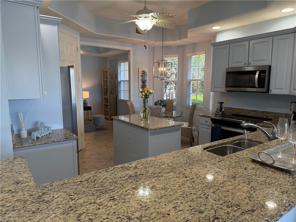 Kitchen featuring a tray ceiling, stainless steel appliances, light stone countertops, a center island, and a ceiling fan