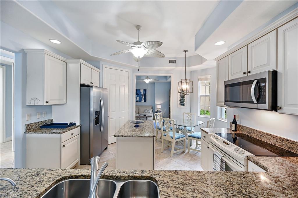 Kitchen with a raised ceiling, stainless steel appliances, light stone countertops, white cabinetry, and a ceiling fan
